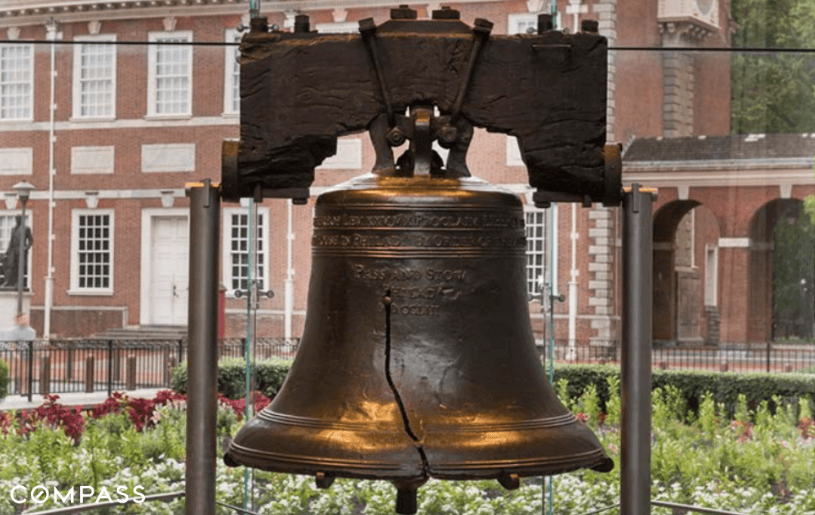 Historic cracked bell displayed in glass enclosure.